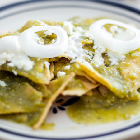 Delicious chilaquiles topped with green salsa, cheese, and onions for a hearty breakfast.