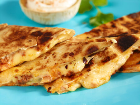 Delicious golden-brown quesadillas with melted cheese and creamy dip, garnished with fresh cilantro.
