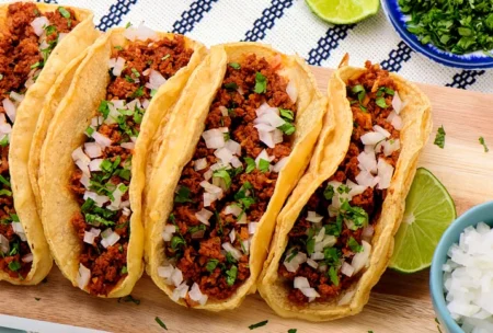 Fresh street-style tacos with seasoned meat, onion, and cilantro on a wooden board.